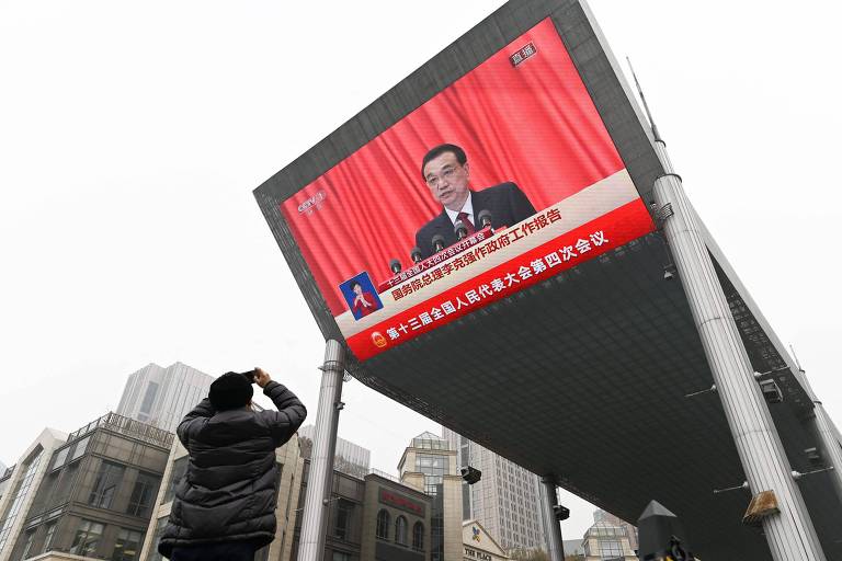 Homem tira foto com celular de tela gigante de TV que transmitia o discurso do premiê chinês, Li Keqiang, em Pequim