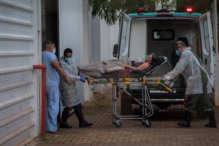 Mulher chega de ambulância em um hospital. Ela está deitada em uma maca e há enfermeiros em volta