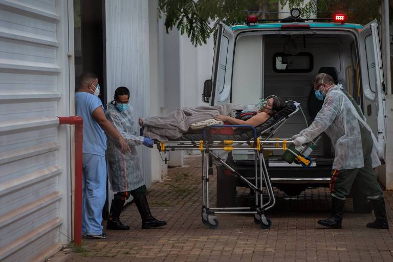 Mulher chega de ambulância em um hospital. Ela está deitada em uma maca e há enfermeiros em volta