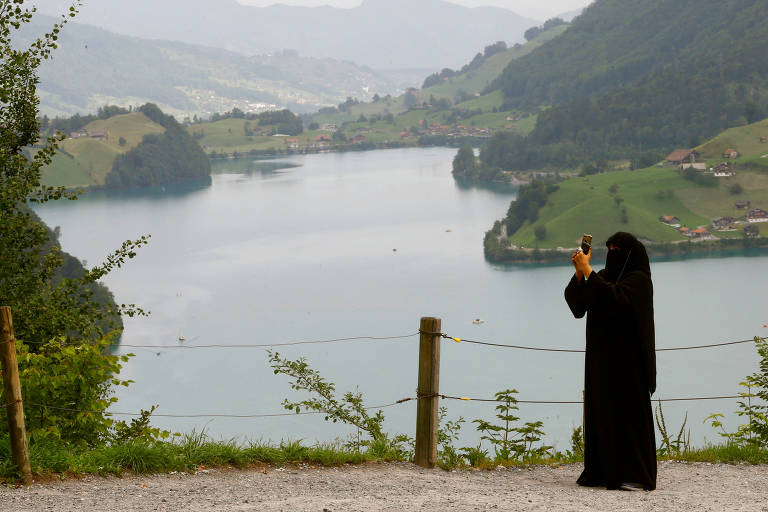 Uma mulher usando um hijab tira uma foto de um mirante acima do lago Lungenersee na Suíça