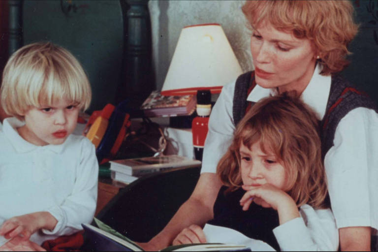 mulher lê para duas crianças enquanto uma delas se esparrama em seu colo