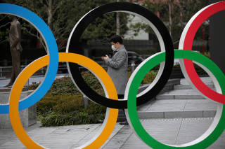 FILE PHOTO: Man looks at his mobile phone next to The Olympic rings in front of the Japan Olympics Museum in Tokyo
