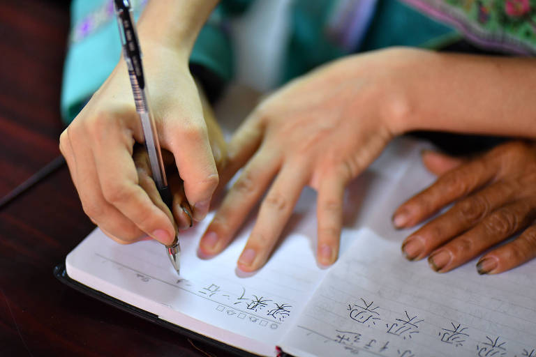 Professor ensina criança a escrever nome em mandarim na vila de Wuying
