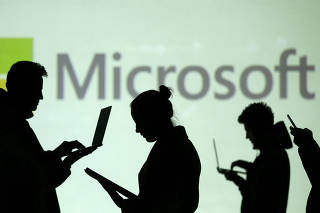 FILE PHOTO: FILE PHOTO: Silhouettes of laptop and mobile device users are seen next to a screen projection of Microsoft logo in this picture illustration