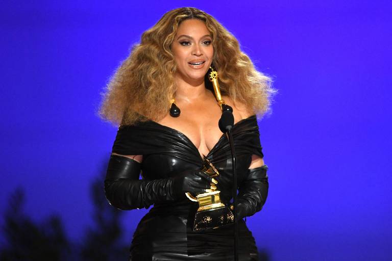 Em foto colorida, mulher com um vestido preto segura um troféu nas mãos em noite de premiação