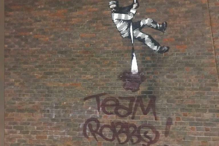 Grafite em parede de tijolos mostra homem descendo por uma corda. Abaixo dele, há as palavras "Team Robbo"