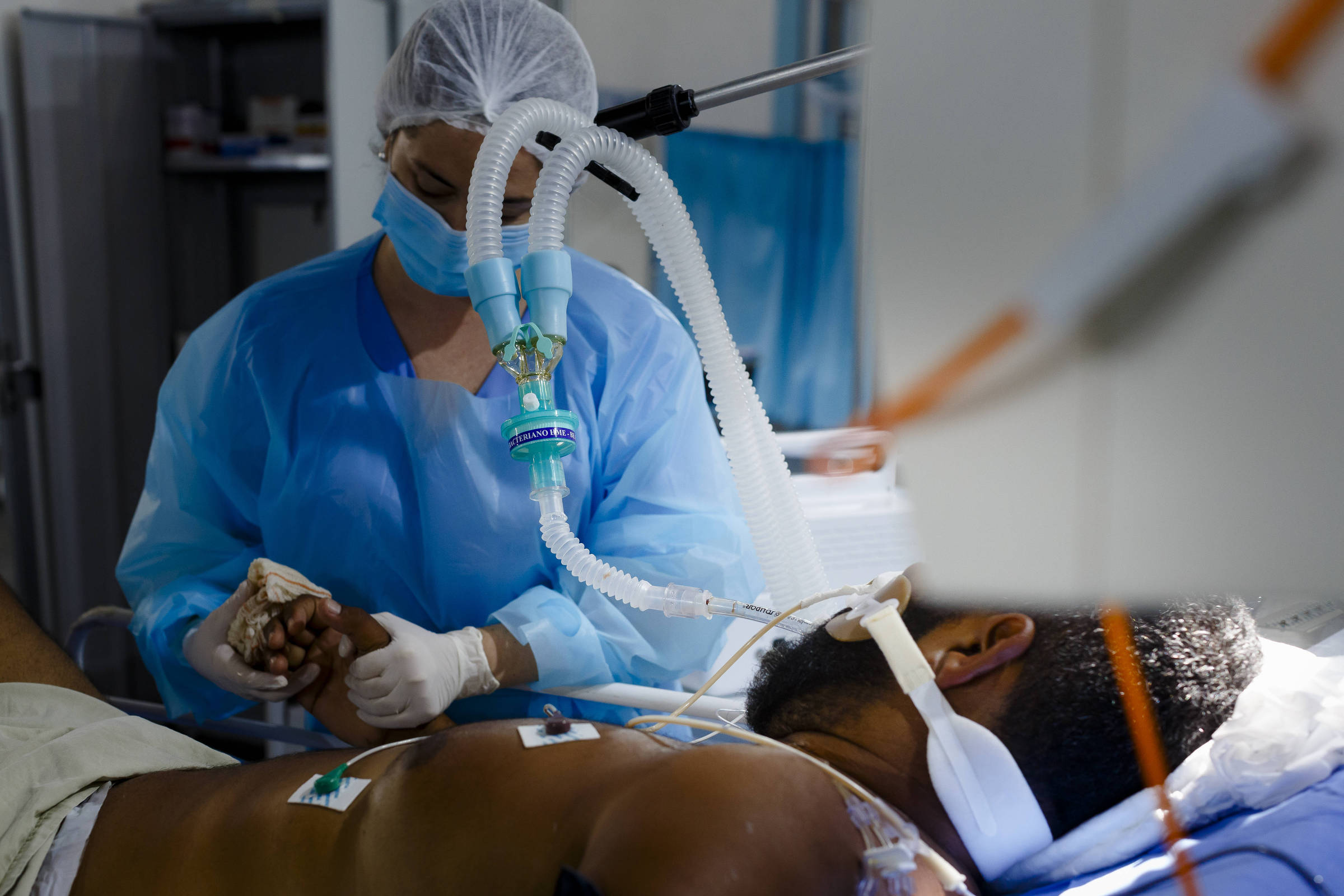 Paciente intubado em cama de hospital sendo atendido por enfermeira.