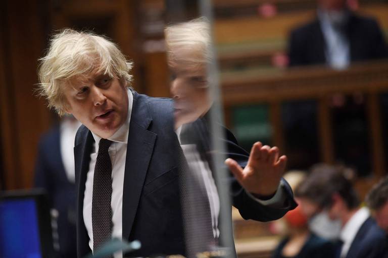 De terno e gravata escuros e gravata branca, Boris gesticula com parte de sua imagem refletida em espelho