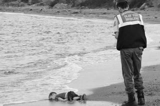 A Turkish gendarmerie stands next to a young migrant, who drowned in a failed attempt to sail to the Greek island of Kos, as he lies on the shore in the coastal town of Bodrum, Turkey