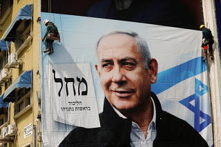 Labourers hang a Likud party election campaign banner depicting its leader Israeli Prime Minister Benjamin Netanyahu ahead of the March 23 ballot, in Tel Aviv