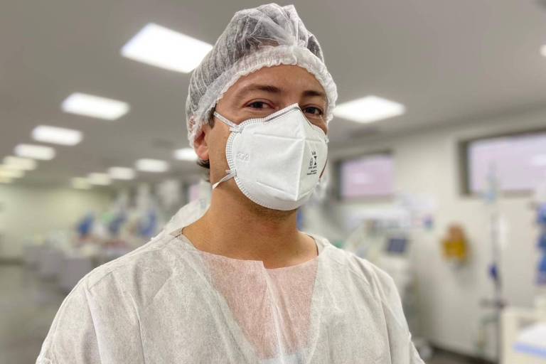médico de máscara, touca e avental hospitalar posa pra foto