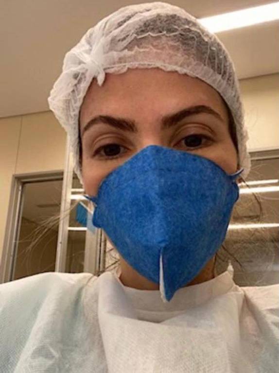 mulher de máscara, touca e avental cirúrgico faz selfie.