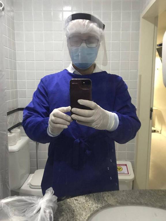 Homem de roupa hospitalar, máscara e gorro faz selfie