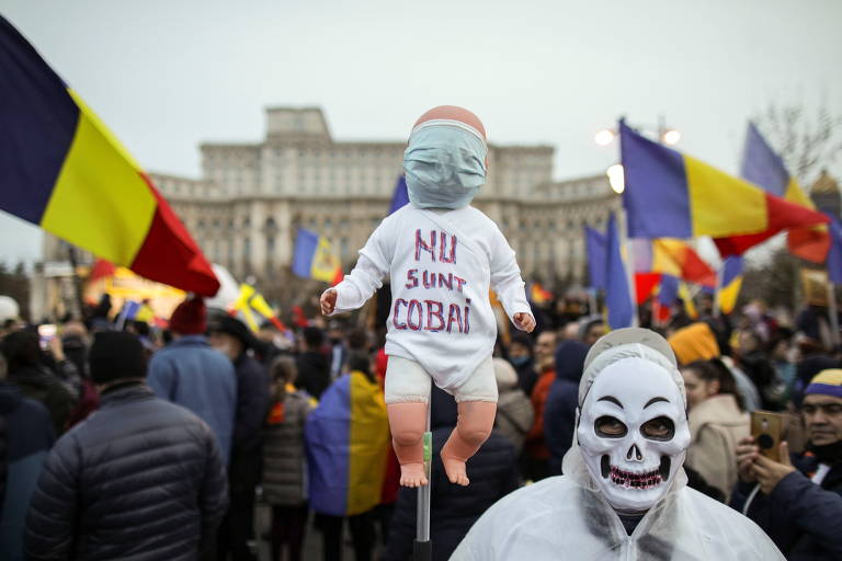 Homem carrega um boneco de bebê com a mensagem 'eu não sou um rato de laboratório' durante manifestação contra uso obrigatório de máscara em Bucareste, na Romênia