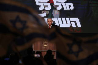 Israeli flags are seen in the foreground as Israeli Prime Minister Benjamin Netanyahu delivers a speech to supporters following the announcement of exit polls in Israel's general election at his Likud party headquarters in Jerusalem