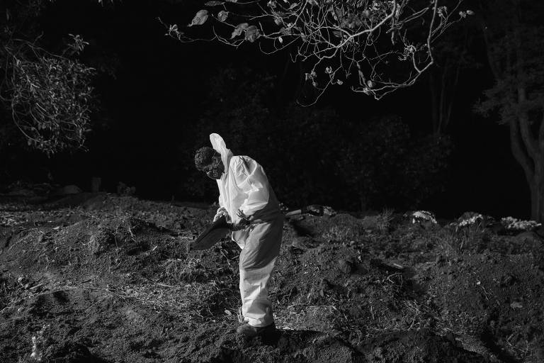 Foto em preto e branco de sepultador que usa traje de proteção contra o novo coronavírus