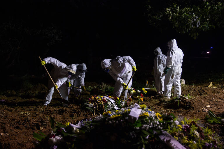 profissionais com traje de proteção completo contra o novo coronavírus fazem sepultamento noturno 