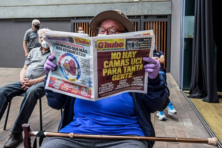 Homem está sentado lendo um jornal; a capa da publicação diz "Não há leitor para tantas pessoas"