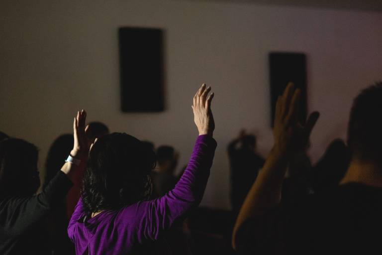 Público em igreja com as mãos para o alto, foto com pouca luz