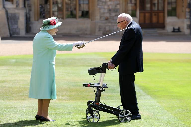 Rainha Elizabeth 2ª usa espada para conferir título de cavaleiro ao capitão veterano Tom Moore, 100, no castelo de Windson; o capitão Tom, como ficou conhecido, arrecadou 32 millhões de libras para o sistema público de saúde ao prometer dar cem voltas em torno de seu jardim