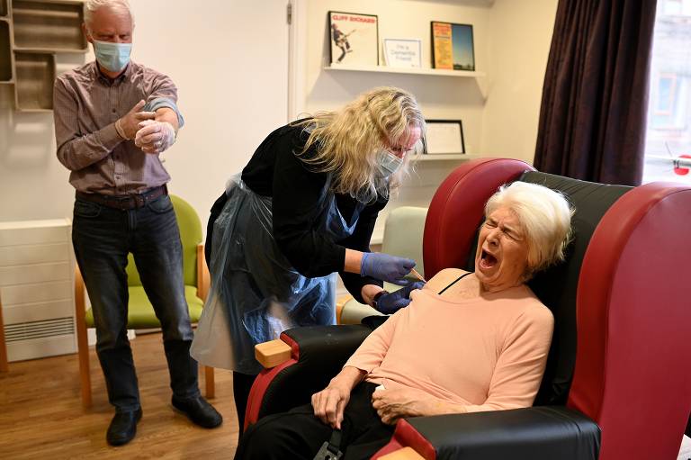 Allan Bishop (em pé), 86, assiste a sua mulher Katleen, 83, receber uma dose de vacina de Oxford-AstraZeneca em casa de idosos em Wigan, na Inglaterra

