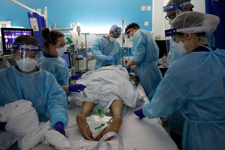 paciente deitado de bruços em maca está rodeado por seis profissionais de saúde que o atendem 