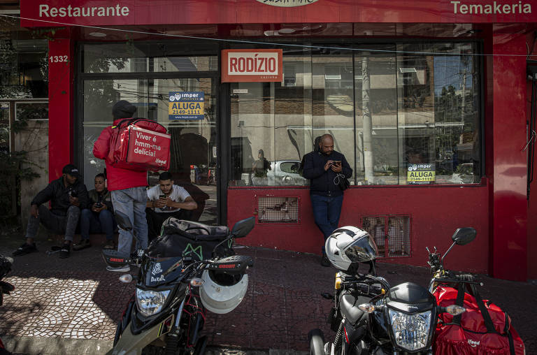 Conhecida por ser um dos bairros mais badalados da cidade, a Vila Madalena sofre uma visível transformação durante a fase mais restritiva de isolamento da pandemia; na foto, motoboys se aglomeram na espera de pedidos de entrega, que também estão rareando 