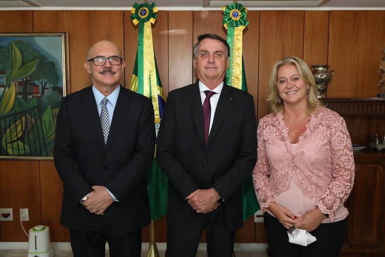 O ministro da Educação, Milton Ribeiro, o presidente Jair Bolsonaro e a presidente da Capes, Claudia Mansani Queda de Toledo, posam lado a lado à frente de duas bandeiras em um gabinete