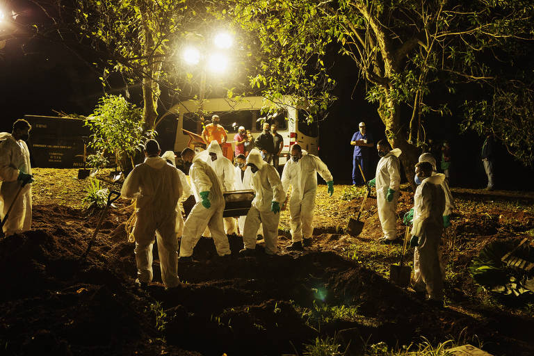 Sepultadores carregam caixão com vítima de Covid-19, iluminados por holofotes, no Cemitério Vila Formosa, na zona leste de São Paulo (SP)