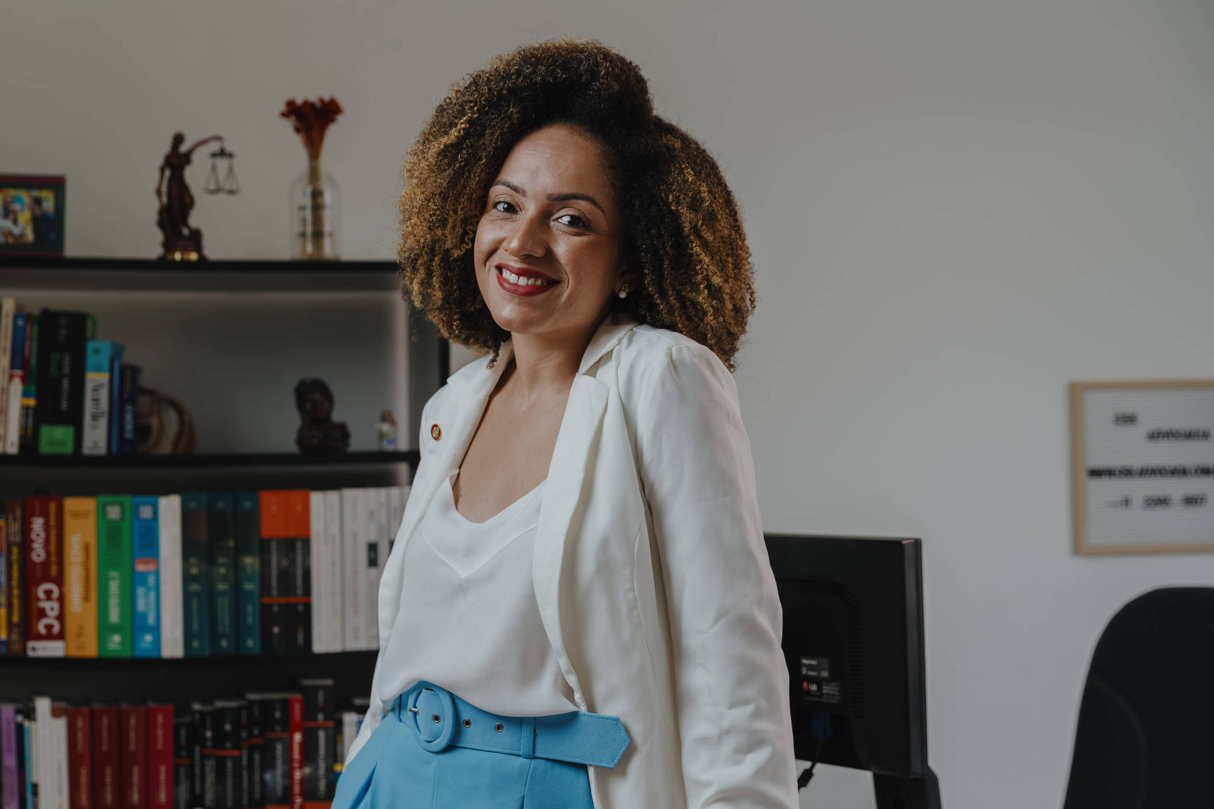 De pé, a advogada autônoma Gabriela Sequeira, com estante de livros ao fundo