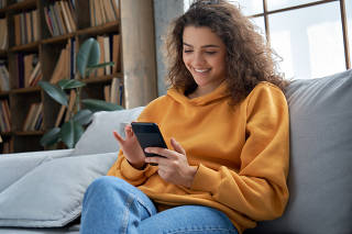 Happy hispanic teen girl checking social media holding smartphone at home.