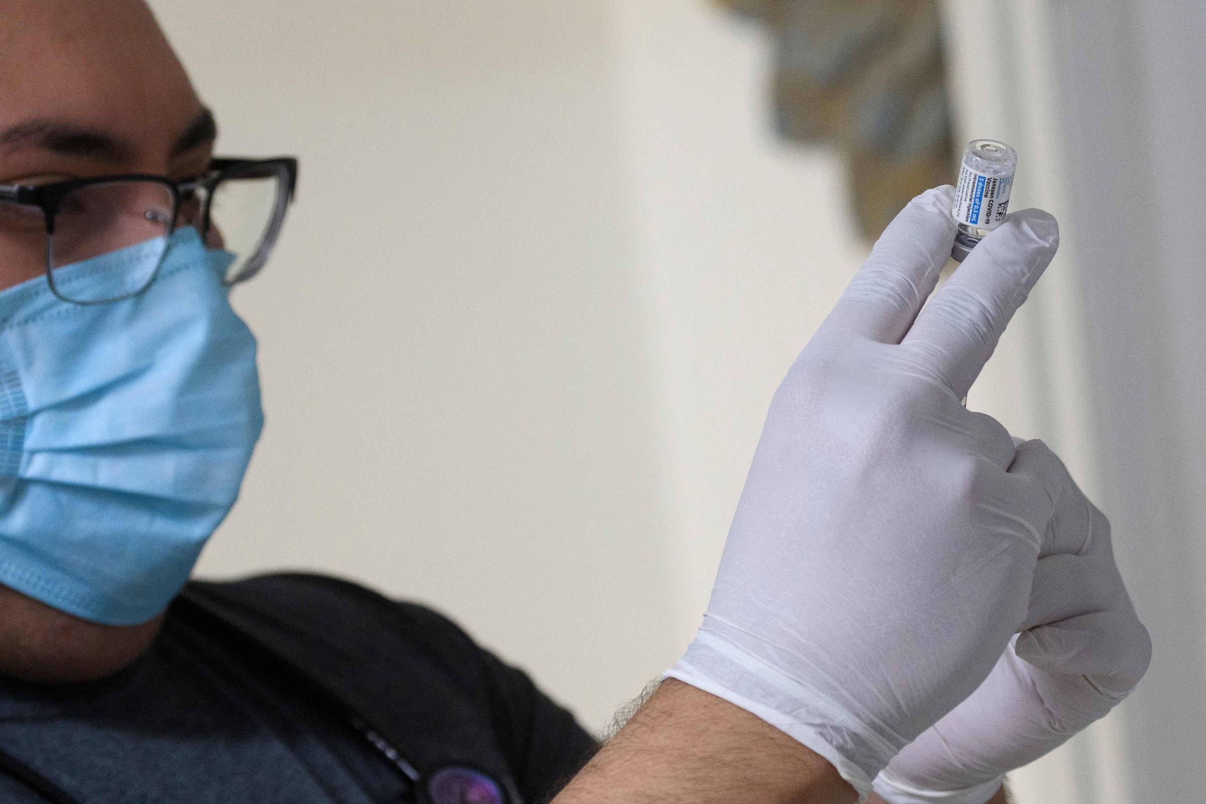 Imagem mostra um homem de máscara, óculos e luvas segurando uma seringa com uma dose da vacina da Janssen
