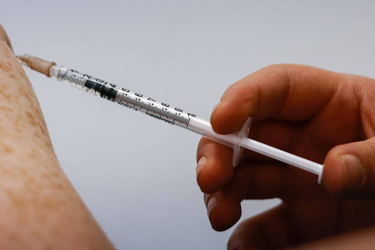 Mão segura seringa e aplica vacina em braço