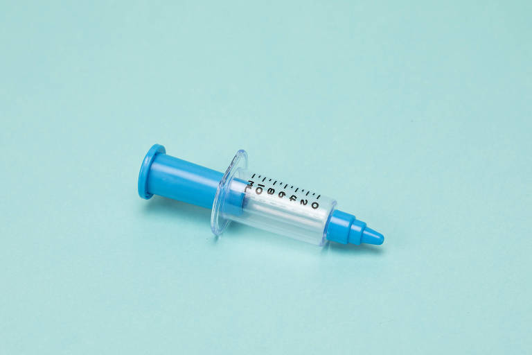 A imagem mostra uma seringa transparente, com detalhes na cor azul, o fundo também é azul, em um tom mais claro