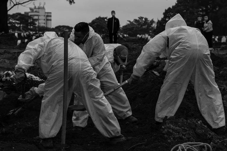 Sepultadores com roupas de proteção enterram vítima de Covid