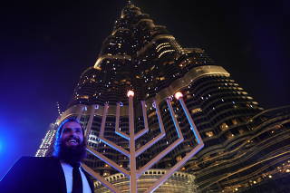 A man stands next to a giant menorah as people celebrate Hanukkah, the Jewish festival of lights, in Dubai