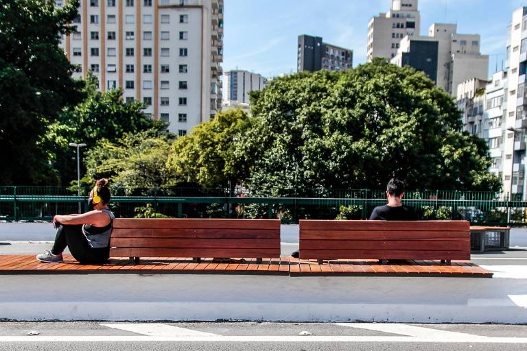 Móveis de madeira instalados no Minhocão; uma pessoa está sentada no móvel apreciando a paisagem urbana de São Paulo