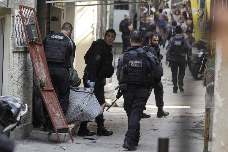 Dois policiais com coletes à prova de balas preto carregam um corpo escondido dentro de um lençol
