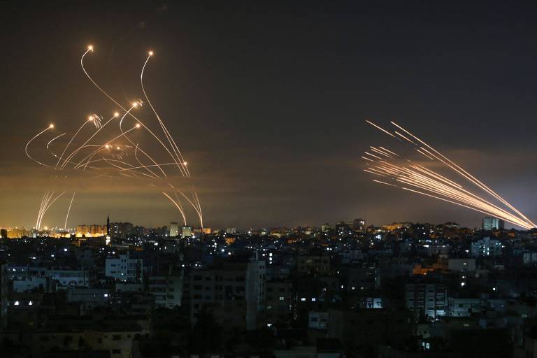 imagem mostra vista noturna de cidade. à direita, diversos mísseis são disparados e riscam o céu. à esquerda, o sistema Domo de Ferro reage para interceptar os mísseis 