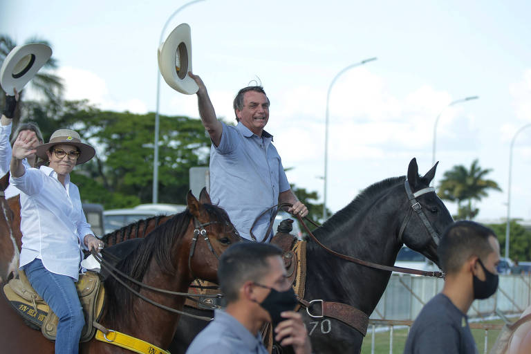Sobre cavalos, Bolsonaro (de chapéu de cowboy na mão) e a ministra acenam para público