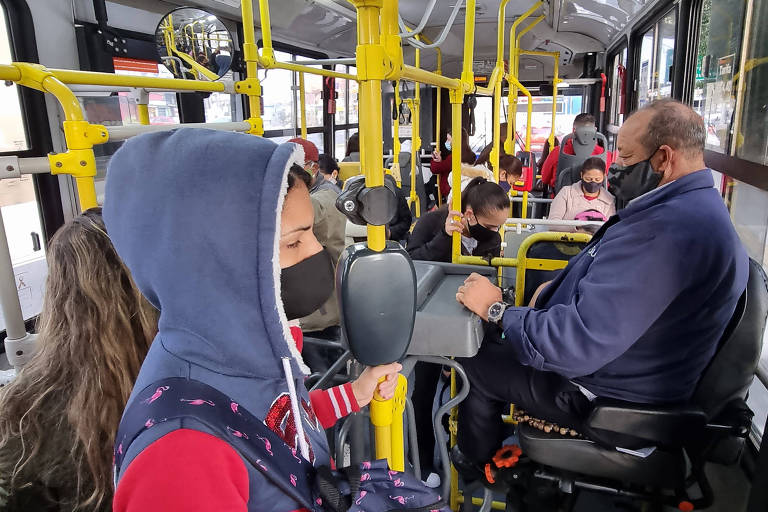 Interior de ônibus municipal na cidade de São Paulo. Imagem mostra cobrador e passageiros 