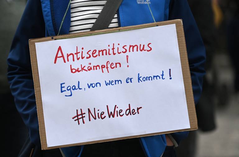 Ativista da Inciativa Contra o Antissemitismo Gelsenkirchen carrega cartaz com a frase "Combata o antissemitismo - não importa de onde ele venha - #nuncamais", em vigília em frente a uma sinagoga de Gelsenkirchen, no oeste da Alemanha, após crescimento de manifestações antissemitas com o acirramento do conflito entre Israel e palestinos
