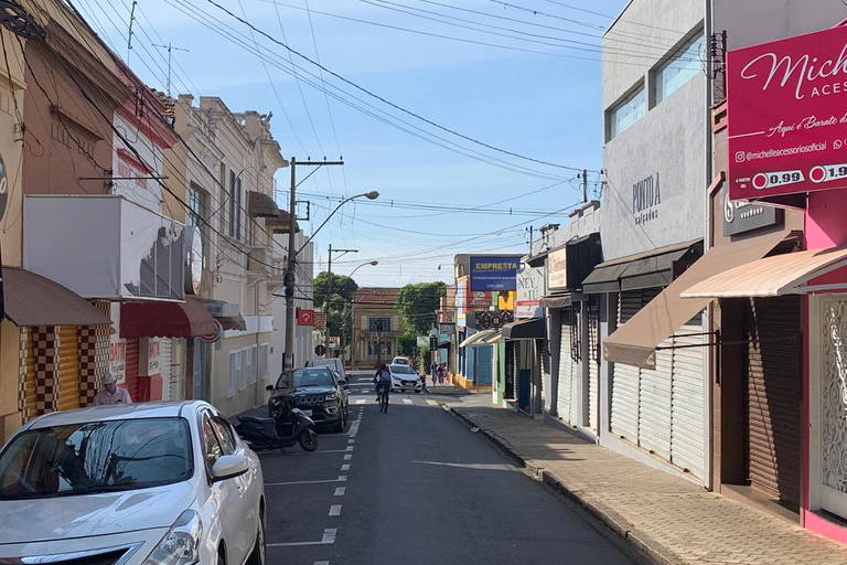 Imagem mostra um carro branco estacionado à esquerda e lojas fechadas