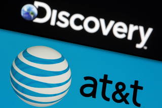 AT&T logo is seen on a smartphone in front of displayed Discovery logo in this illustration