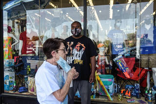 A woman puts on her face mask as she walks by a man wearing a face mask in front of a store in the Staten Island borough of New York on Wednesday, May 19, 2020. (Stephanie Keith/The New York Times)