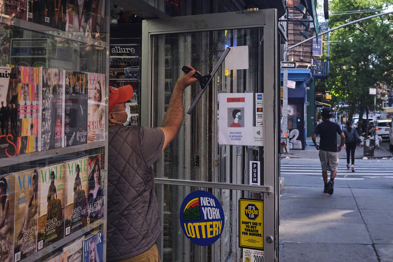 Trabalhador limpa janela em banca de jornais em Manhattan