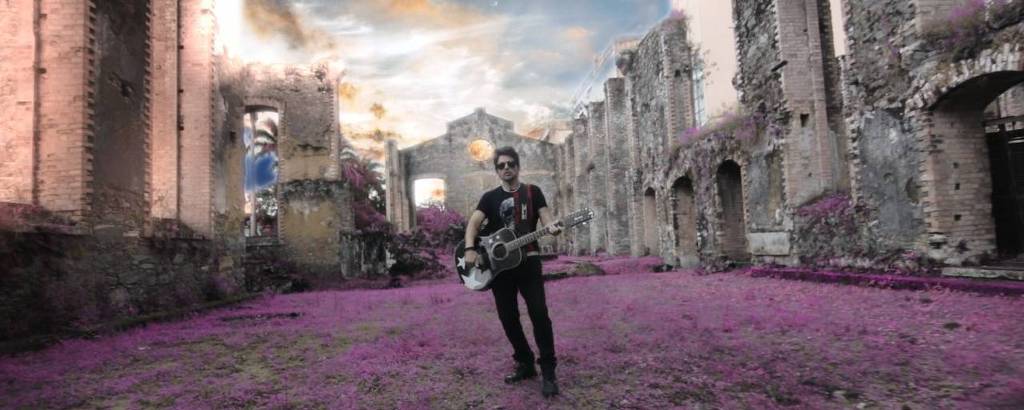 Homem vestido de preto segurando uma guitarra com o chão coberto de pétalas rosas