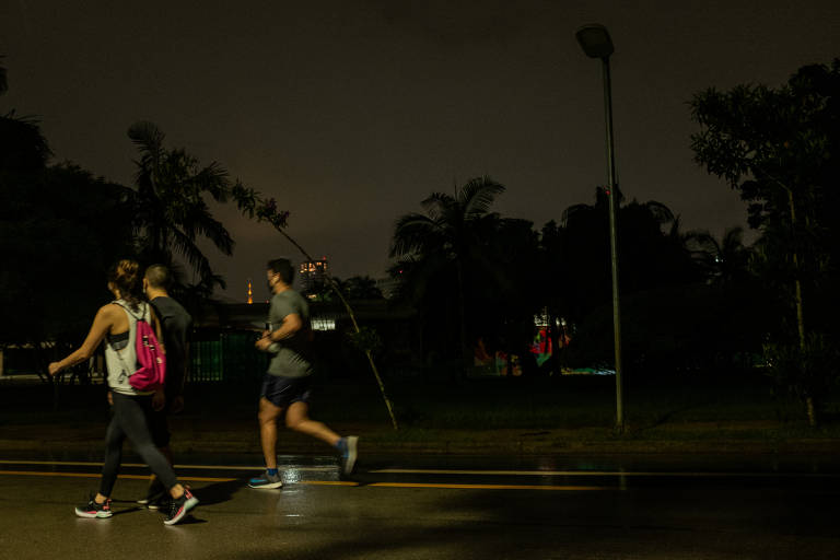 Duas pessoas caminham e outra corre no Parque Ibirapuera a noite