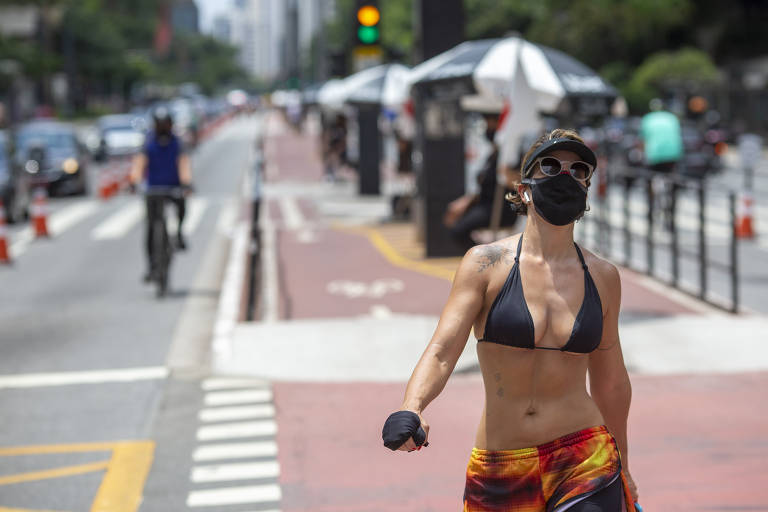 Em destaque, mulher de máscara caminha em uma rua
