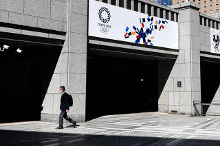A man wearing a protective face mask walks past  banners of the Tokyo 2020 Olympic Games outside the Tokyo Metropolitan Government building in Tokyo last year on March 25, 2020. (Noriko Hayashi/The New York Times)